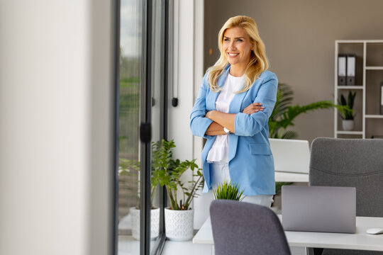 Confident professional woman smiling in modern office while looking out the window