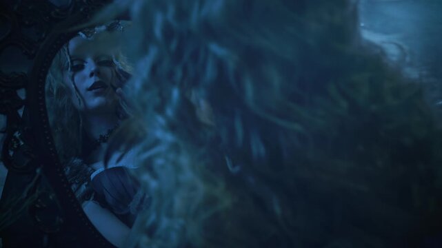 Fantasy character fashion model looking at reflection in magical mirror posing in dark night forest moon light. evil gothic fairy woman bird costume. sexy face eyes lips fairy tale elf girl art video
