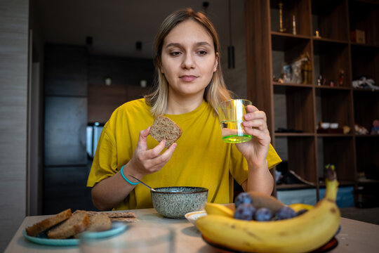 Woman holding a slice of whole-grain bread and a glass of water for a healthy breakfast. Mindful eating, morning nutrition, and wellness routine.