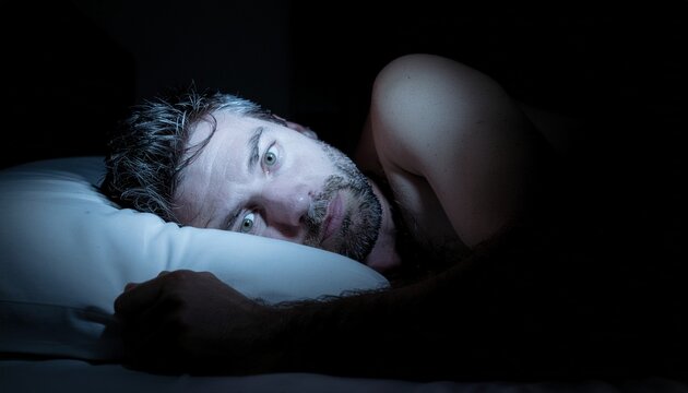 Close up of sad disappointed man lying awake in bed staring blankly at night with endless mind rumination and insomnia disorder