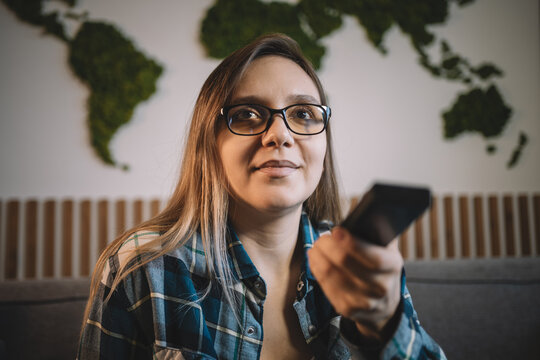 woman has switched channels with the remote control and is looking at the TV screen with interest. television, watching movies and TV series