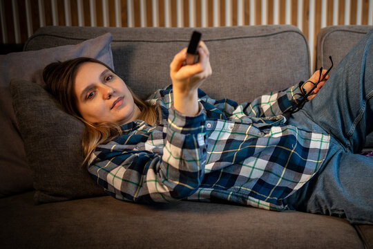 Happy woman, popcorn and laughing or watching tv with remote control for television in living room at home. Subscription, comedy and girl on couch for streaming movie, show or funny video to relax