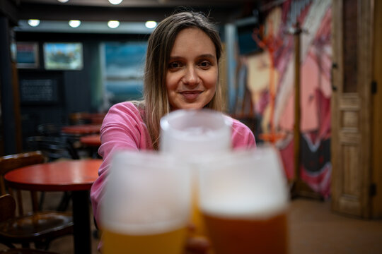 Friends clinking glasses of light beer in a pub. Smiling young woman enjoying a social gathering with refreshing draft beer. Cheers For Us. women Drinking Draft Beer And Clinking Glasses