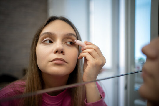 Woman applying light eyeliner or concealer to her eyelid in front of a mirror. Eye makeup, beauty routine, and cosmetic enhancement.