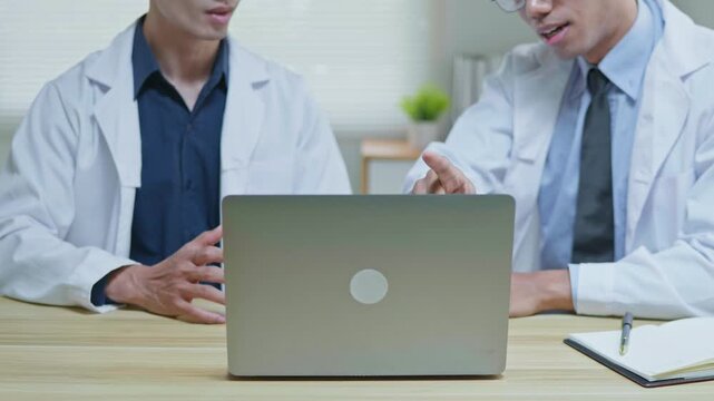 Doctors discussing a medical case together in a modern clinic office, using a tablet and laptop for telehealth, healthcare technology, medical consultation and health insurance planning.