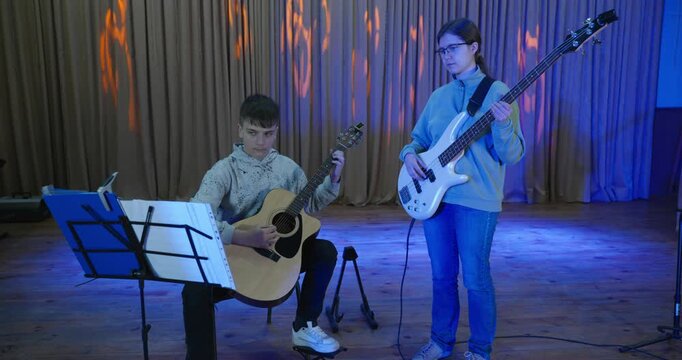 Boy and Girl Practice Playing Music on Stage. Kids Play Guitar and Bass Guitar. 4K 10-bit