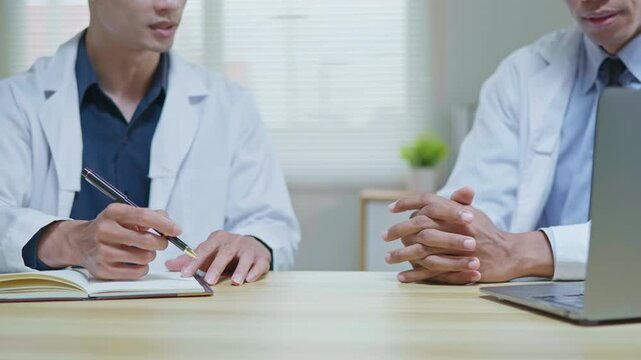 Doctors discussing a medical case together in a modern clinic office, using a tablet and laptop for telehealth, healthcare technology, medical consultation and health insurance planning.