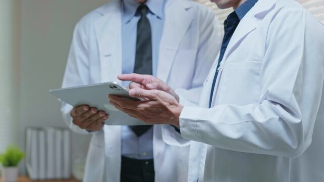 Doctors discussing a medical case together in a modern clinic office, using a tablet and laptop for telehealth, healthcare technology, medical consultation and health insurance planning.