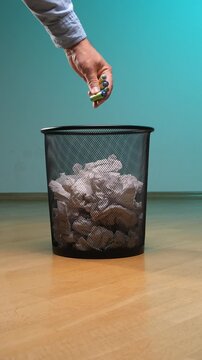 Vertical video person's hand dropping several used batteries into a metal waste bin filled with crumpled paper, highlighting themes of waste management, responsible disposal, and environmental concern
