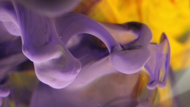 The movement of purple and yellow ink slowly diffusing in water. This "ink-in-water" effect creates dynamic, graceful, and colorful cloud- or smoke-like plumes.
