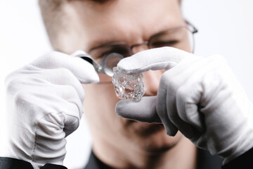 Fototapeta premium Male jeweler inspecting raw diamond with magnifier and gloves