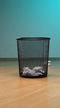 Vertical video crumpled paper actively falls into a black mesh waste bin, symbolizing discarding failures, making a fresh start, ending, or cleaning up in an office or home environment