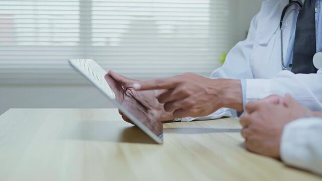 Doctors discussing a medical case together in a modern clinic office, using a tablet and laptop for telehealth, healthcare technology, medical consultation and health insurance planning.