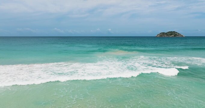 Turquoise ocean waves meet a white sandy shore backed by green hills under a partly cloudy sky. Seychelles, Mahe.
