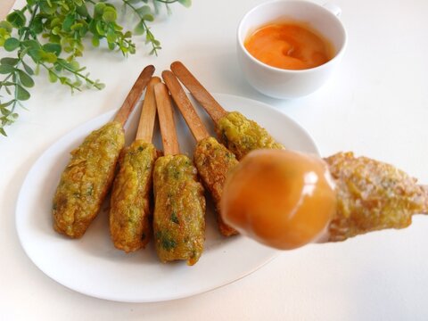 Traditional Indonesian street food called sempol ayam made from minced chicken, tapioca flour, spices, and egg coating. Fried chicken skewers served on a white plate with sweet chili dipping sauce