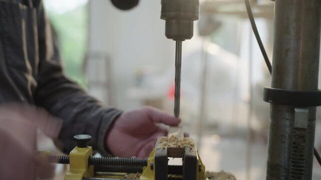 Craftsman drills wood in workshop vise during carpentry and woodworking process in natural light
