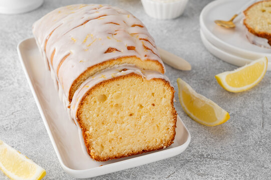 Lemon loaf cake with sugar icing on a white plate on a stone background. Copy space.
