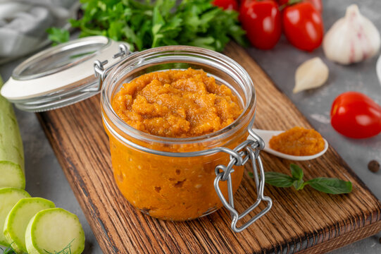 Zucchini caviar in a glass jar with fresh vegetables and herbs on a rustic board, homemade vegetable spread for healthy eating and canning.