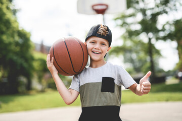 Fototapeta premium portrait of a boy kid playing with a basketball in park