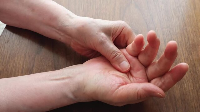 Close Up of Senior Woman Massaging Her Hands at Wooden Table