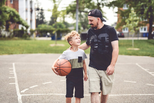 man and young boy playing basketball on a court, teaching little player and spending time outdoors