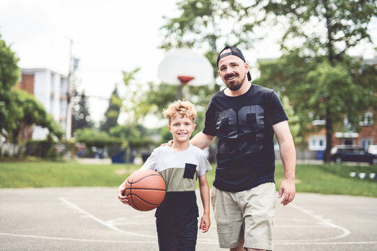 man and young boy playing basketball on a court, teaching little player and spending time outdoors