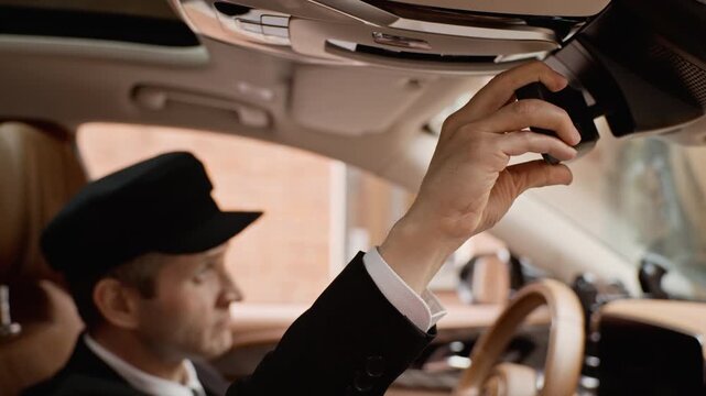 Middle aged Caucasian chauffeur adjusting rearview mirror inside luxury vehicle. Footage is perfect for promoting premium private driver services and high-end transport business marketing