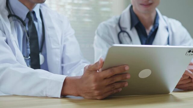 Doctors discussing a medical case together in a modern clinic office, using a tablet and laptop for telehealth, healthcare technology, medical consultation and health insurance planning.