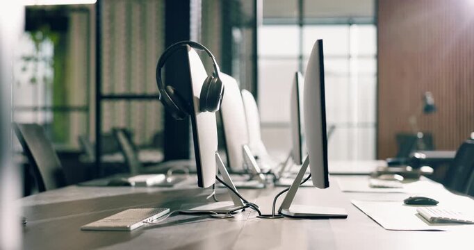 Workplace, equipment and computer with headset in call center agency for virtual assistance. Empty, space and technology with lens flare or help desk for business operations or startup in office
