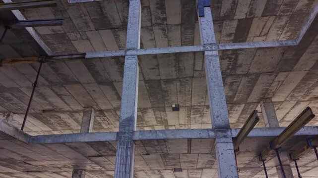 Underside of concrete ceiling grid in unfinished building. Low angle view shows crossing beams, wooden supports and rough weathered surfaces.
