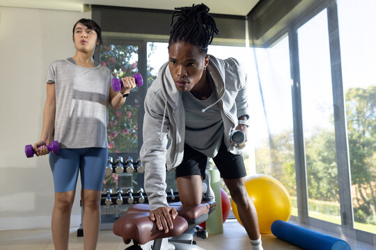 African American duo training in home gym, man doing row on bench, woman holding purple weights