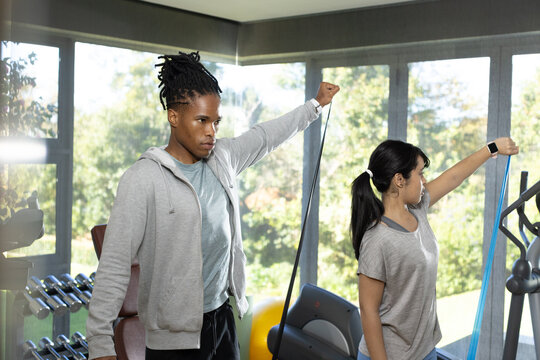 African American pair exercising with bands in gym near weights and smartwatch wearing sportswear