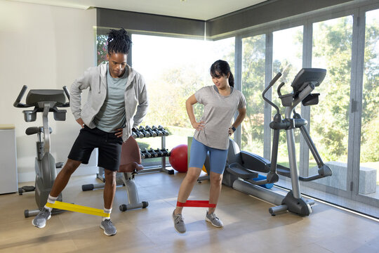 Diverse workout partners performing lateral steps with loop bands in home gym in athletic wear