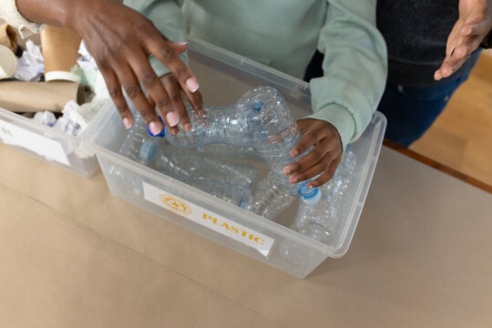 Community volunteers sorting clear bottles into transparent bin labeled PLASTIC at workshop table