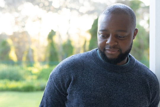 Mature man leaning on white post on porch, facing garden, wearing dark gray sweater, copy space