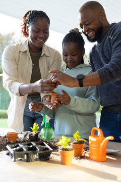African family with child planting seedlings on porch with terracotta pots, soil, watering can