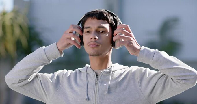 African American man lifting headphones and adjusting them to listen outdoors, closing eyes briefly