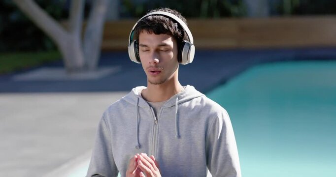 African American man early-20s wearing hoodie and headphones, closing eyes and praying poolside