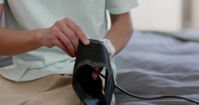 Man seeing black cuff on bed, picking up, sliding left arm inside, fastening strap readying monitor