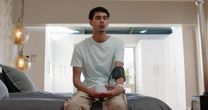 African American man on bed, wearing BP cuff, holding monitor, awaiting reading after cuff pumping