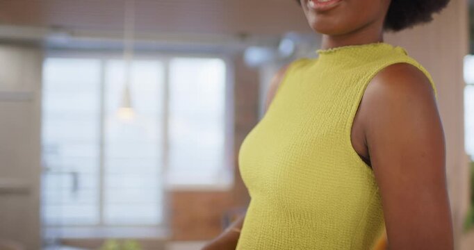 African woman resting on counter in loft, wearing smartwatch, pivoting toward camera, engaging