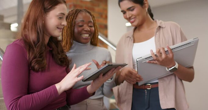 Diverse female coworkers opening tablet and tapping screen at stairs, reviewing content together
