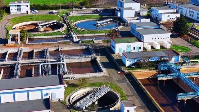Circular sewage tanks and buildings. Drone angle of clarifier basins, walkways, white utility buildings and access roads.