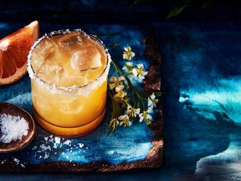 Paloma cocktail with tequila, fresh grapefruit juice, served in a salt-rimmed glass with ice and grapefruit wedge 