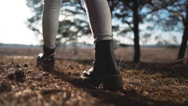 Person hiking on forest trail with boots stepping on dirt path. Hiker walks through wooded nature area. Hiking footwear moves along outdoor trail. Boots trek on natural forest ground surface.