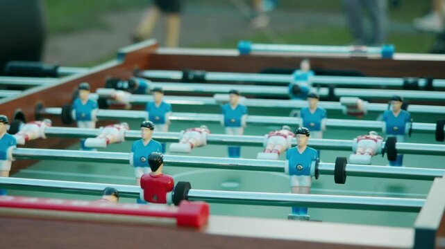 Close up captures foosball table during lively outdoor summer party with crowd enjoying game. Colorful table football match creates fun atmosphere at open air festival.