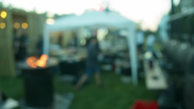 Blurred barbecue cooking area is visible at outdoor street food festival. Burning grill creates warm atmosphere during evening event.