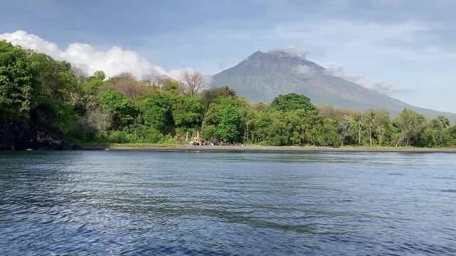 Volcanic rocks and green trees on the beach with Mount Agung background on a calm sunny day