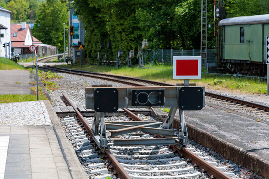 Steel buffer stop with red signal plate at the end of a railway track on concrete sleepers, railway safety concept.