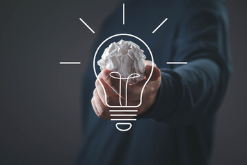 Hand holding crumpled paper with light bulb icon representing creativity, innovation, problem solving, brainstorming, startup ideas, business inspiration, and creative thinking concepts. © Bordinthorn